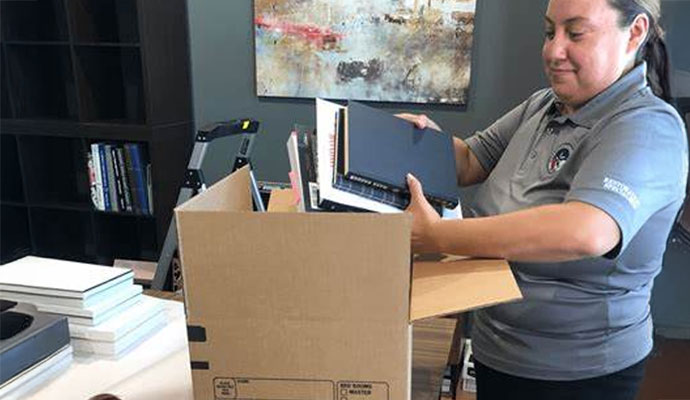 A restoration professional packing books and documents into a cardboard box